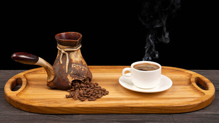 Freshly brewed hot black coffee in a white cup on a wooden board next to a ceramic turkey with coffee beans.