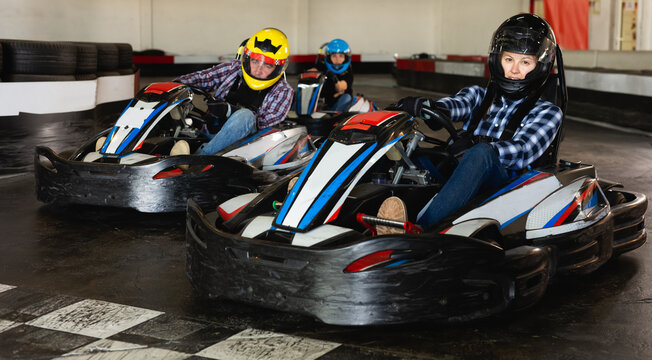 Young positive people in helmets driving racing cars in karting club