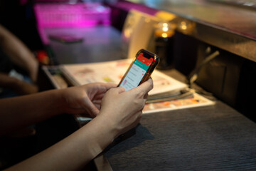 Close-up at person's hand is holding a smartphone to play on social media, shopping online or do the business during waiting a food on the restaurant's counter bar. Social addict concept photo.