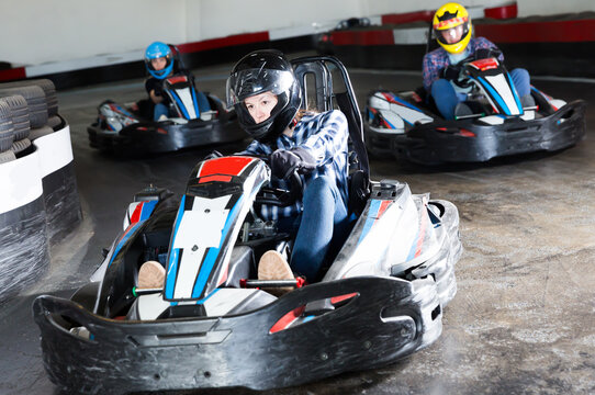 Happy people in helmets driving cars for karting in sport club indoor