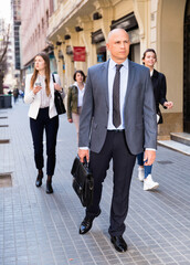 Confident cheerful positive businessman in formal suit walking on city street to office at rush hour
