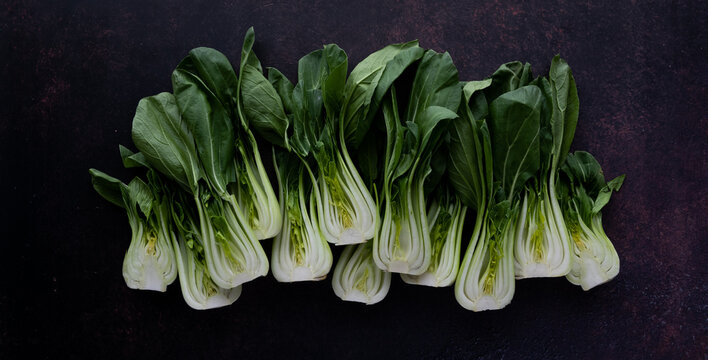 Many bok choy clusters in a row against a dark background.