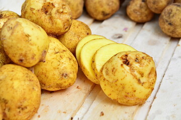 Heap of natural yellow potatoes and cutting chips on wooden plank on blurred background of fresh tubers