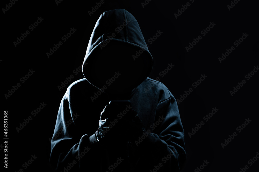 Poster hacker using smartphone. men in black clothes with hidden face looks at smartphone screen on black b