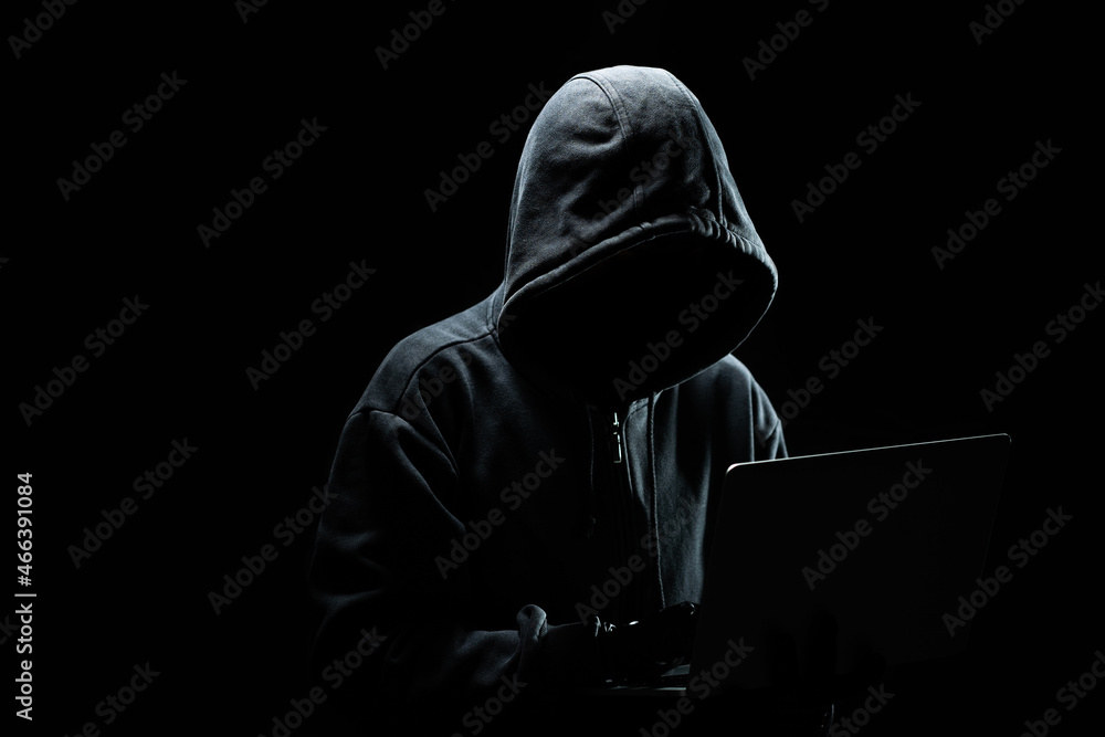 Poster hacker without a face in a hood on with laptop in the dark