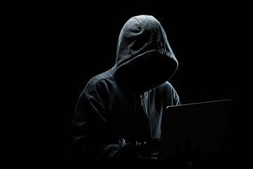 Hacker without a face in a hood on with laptop in the dark