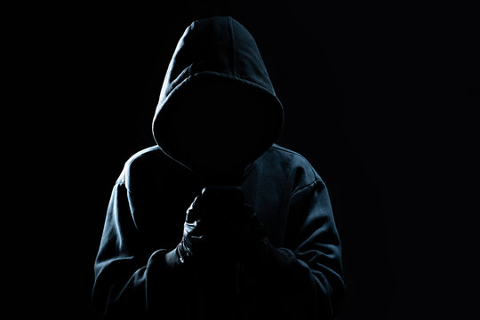 Hacker Using Smartphone. Men in black clothes with hidden face looks at smartphone screen on black background