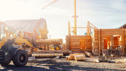 Loader carries logs against background of building wooden house