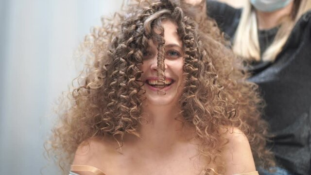 Close-up of a beautiful woman with curly hair, her hair is being done, she blows on a strand of hair looking at the camera. High quality 4k footage