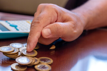 Counting brazilian money, real coins. Calculator and pen in blurred background.