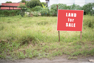 Land for sale sign. Red sign for sale plot. Green lawn behind sign. Land for sale signboard on...