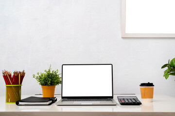 Laptop computer with blank screen, home plant, watering can, unrecognizable picture in frame on...