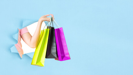 female hand holding shopping bags blue background Break through the torn blue wall.season sale and shopping .