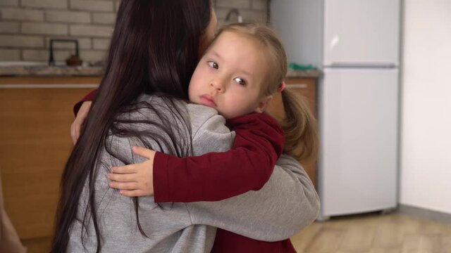 A Sad Daughter Hugging Mother at home. Back View of the Brunette Mom with Her Kid, Little Girl with Frustrated Face Embracing Young Woman