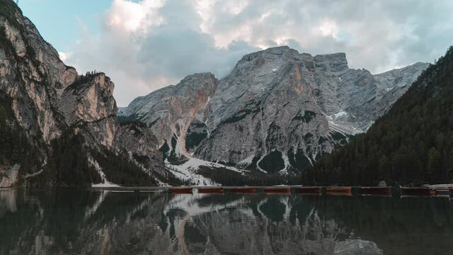 Timelapse of a sunset from Lake Braies on a summer day with few clouds. Large mountains can be seen in the background and the lake with the clear water and boats in the foreground.