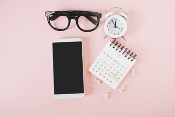 mock up of white mobile phone included clipping path on touchscreen, with calendar, analog alarm clock, thumbtacks and eye glasses on sweet pink background
