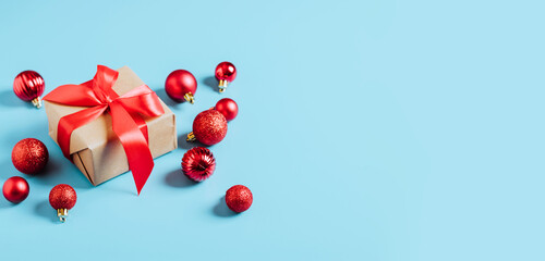 Beautiful Christmas red balls and New Year's gift with a red ribbon decorating toys on blue background. New Year Christmas concept. Flat festive mockup with copy space