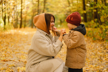 Happy young mother and son are walking in the autumn forest. Autumn outdoor activity for family with kids. Happy mother's day. Family day. Autumn day. Happy family leisure.