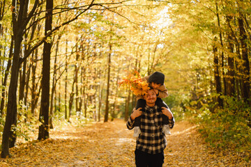 Fototapeta premium Happy young dad and son are walking in the autumn forest. Autumn outdoor activity for family with kids. Happy father's day. Family day. Autumn day. Happy family leisure.