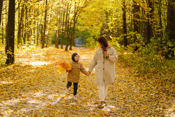 Fototapeta premium Happy young mother and son are walking in the autumn forest. Autumn outdoor activity for family with kids. Happy mother's day. Family day. Autumn day. Happy family leisure.