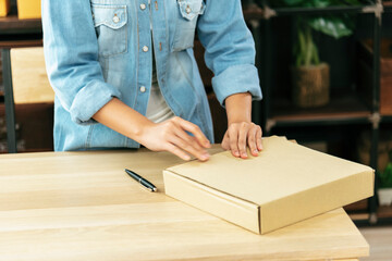 Woman packing box on table checking goods package delivery shipping to customer. Asian woman startup small business at home office desk. Entrepreneur asian woman packing product for delivery items