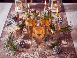 Silver candles, lights, cones, glasses of champagne, Christmas decorations on the table.