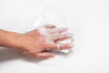 Hand with foam holding sponge, cleaning white surface