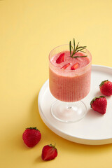 Strawberry smoothie in a cocktail glass with strawberry in a white dish decoration with yellow background for food advertising , front view