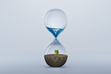 Hourglass with fresh water drop to green plant planting on dry land isolated background, metaphoric...