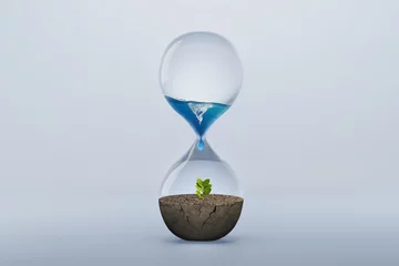 Gordijnen Hourglass with fresh water drop to green plant planting on dry land isolated background, metaphoric of saving water, Drought and Climate change. © piyaset
