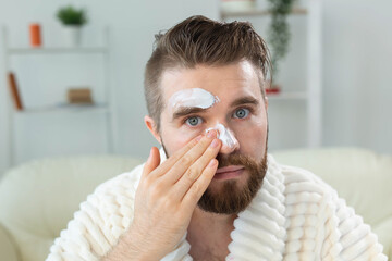 Bearded guy applying anti-wrinkle cream on his face. Skin care and spa for man concept.