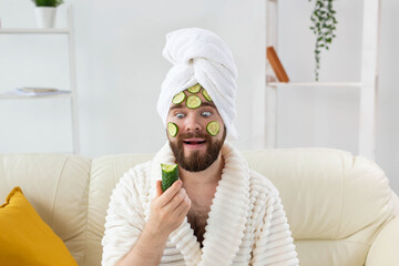 Funny bearded man holding cucumber slices on the face. Spa at home, body and skin care for male...
