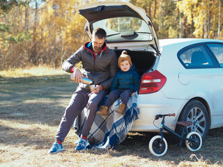 Fototapeta premium young beard man having a picnic in the trunk with his son; autumn