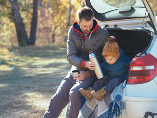Cute toddler boy in casual clothes having a picnic with his dad in the trunk