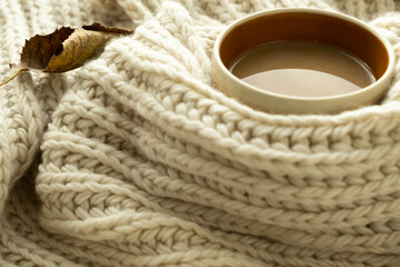 Cup of autumn coffee, tea or hot chocolate, fall leave on a warm scarf. Drink for autumn cold rainy days. Seasonal, morning coffee. Sunday relaxing, hygge, still life concept. Selective focus