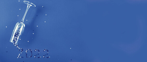 Champagne glass with star shaped sequins in the form of inscription 2021 on a blue background.