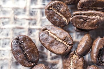 Fototapeta premium Coffee bean grains standing on straw fabric. macro photo. 