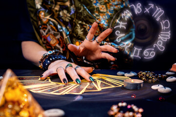 A witch spread out her tarot cards on the table. Hands close-up. The zodiac circle in the upper...