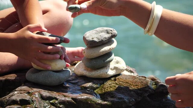Woman bilds stones pyramid on the seashore on a sunny day on the blue sea background. Happy holidays. Pebble beach, calm sea, travel destination. Concept of happy vacation on the sea, meditation, spa