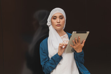 Portrait of an Arab student girl holding a tablet. Arab business woman in hijab holding a tablet in the street. Woman is dressed in hijab
