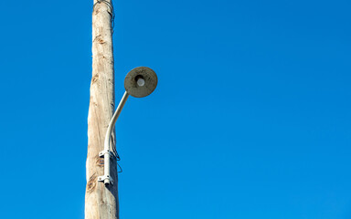 Retro streetlight, bulb hanging on wooden electric pole. Vintage pillar lamp, blue sky background