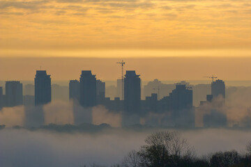 Foggy view of the morning city. Fiery dawn in Kiev. Buildings in the fog