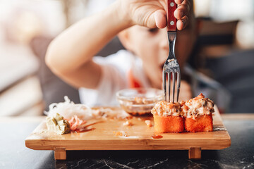Boy enjoys eating sushi rolls in outdoor cafe