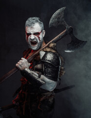 Naklejka premium Screaming mythical warrior with painted skin and axe in studio