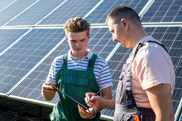 workers stand near solar panels and look  at notebook