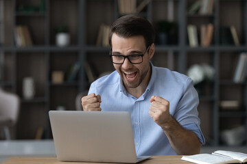 Overjoyed young businessman manager in glasses celebrating online lottery auction betting win,...