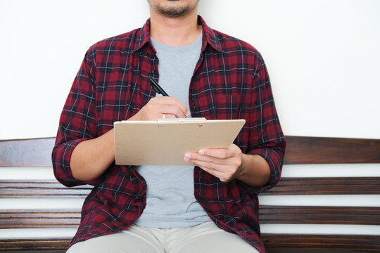 A guy sitting in a bench while taking notes