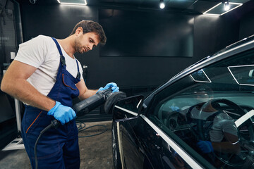 Male mechanic with grinding machine polishing car mirror