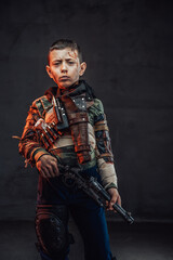Preschool boy in ragged clothes holding pistol in dark background