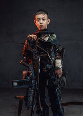 Naklejka premium Young boy in ragged clothing with shotgun in dark background